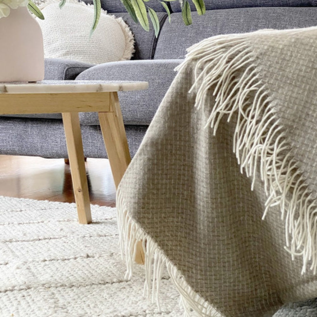 Chiswick Beige Merino Wool and Cashmere Throw casually draped over a couch in a cosy living room setting, enhancing the home's decor.