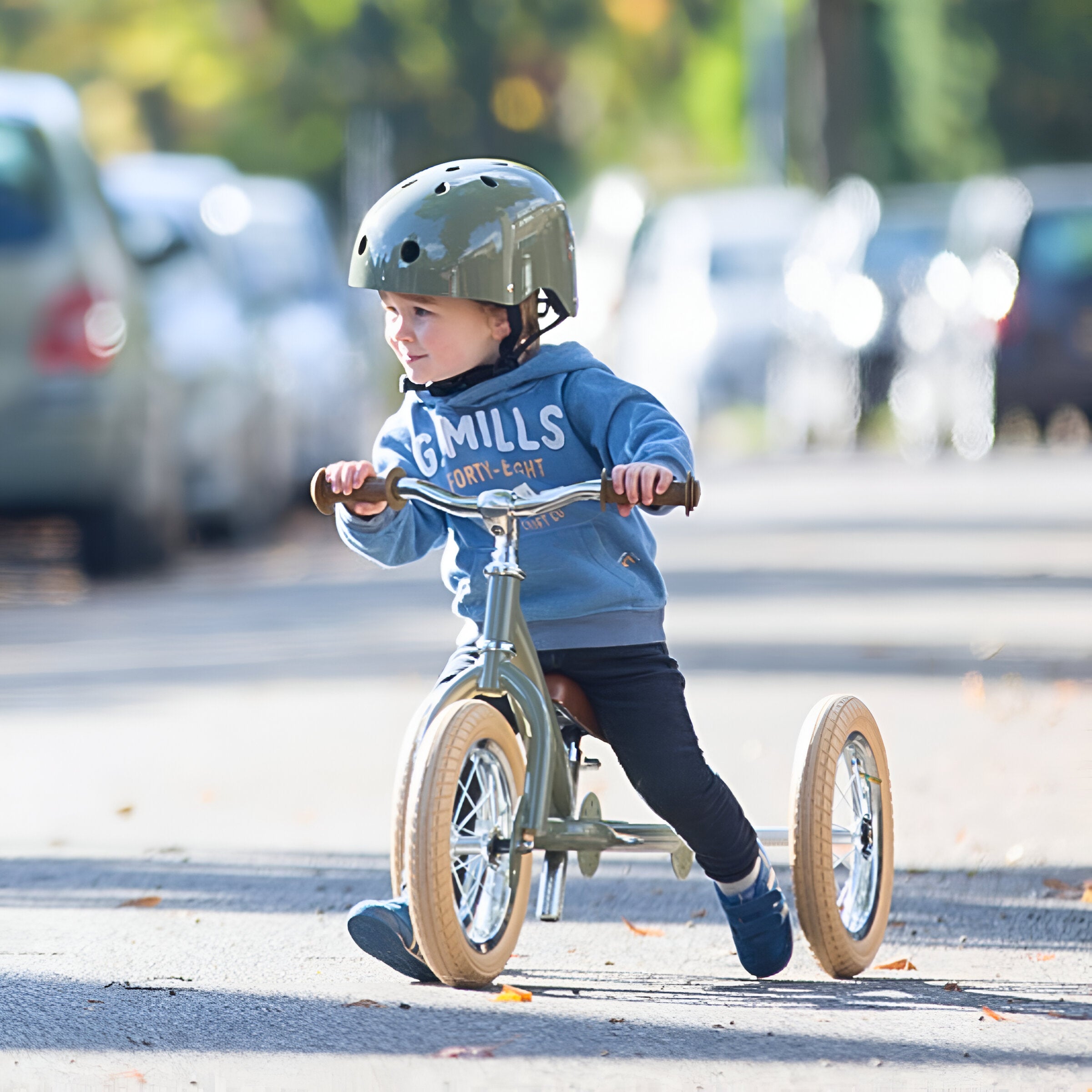 Active kid riding the Trybike Vintage Green balance bike on urban street.