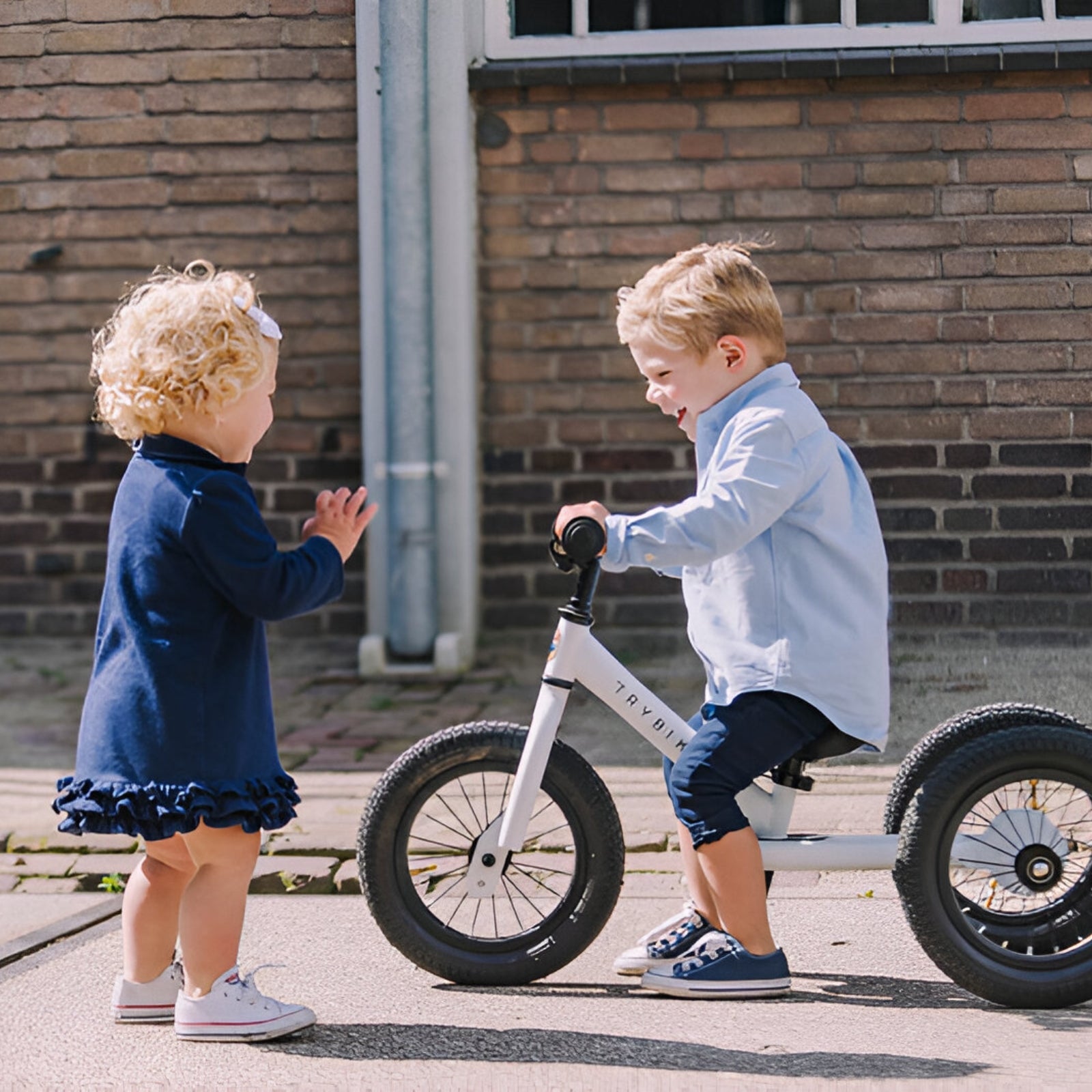 Child learning to ride on a White Trybike balance bike in urban setting.